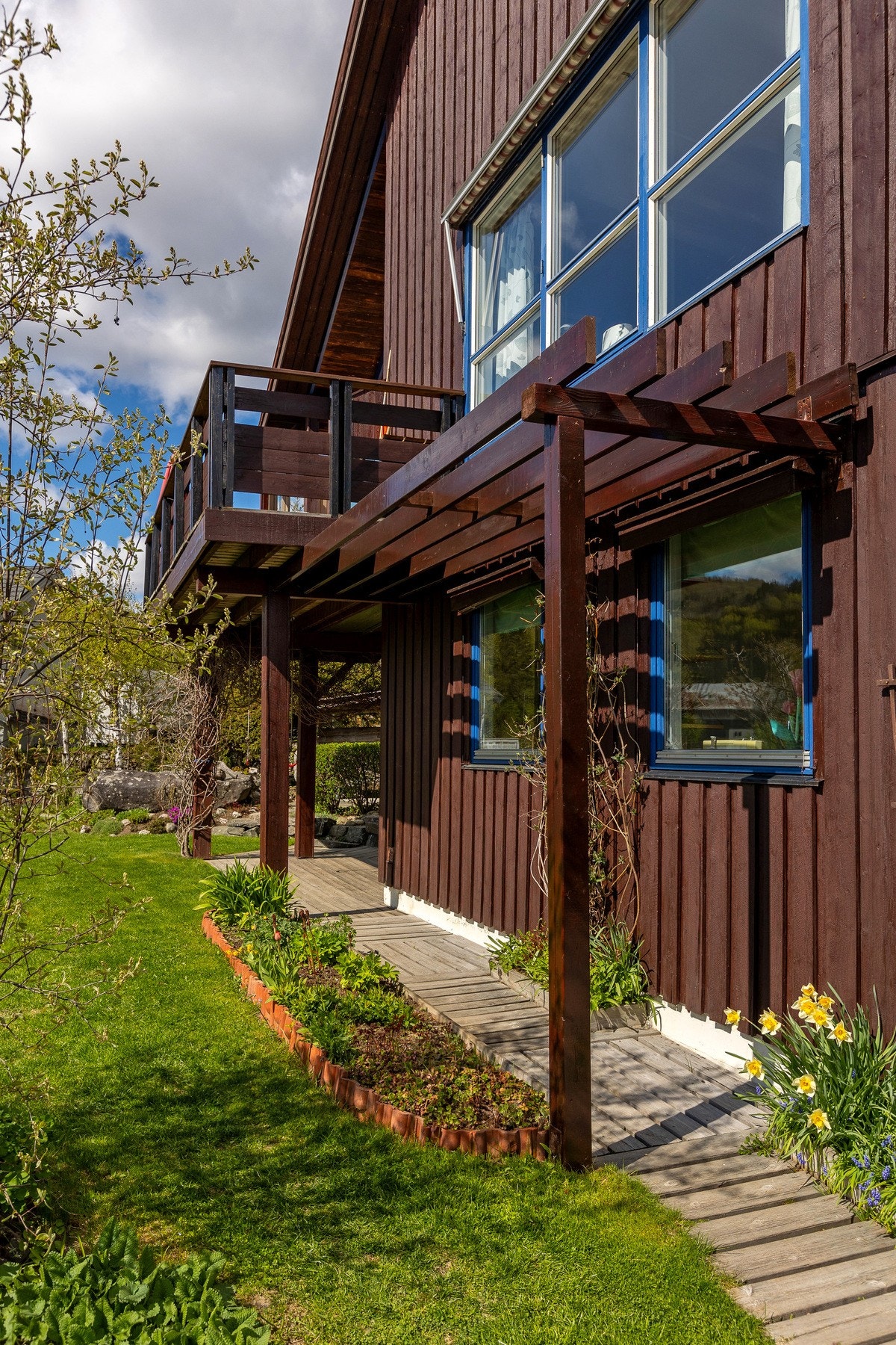 Boligen har en innbydende fasade med lune uteplasser, pergola og flotte detaljer som skaper et hyggelig uterom. Galleribilde