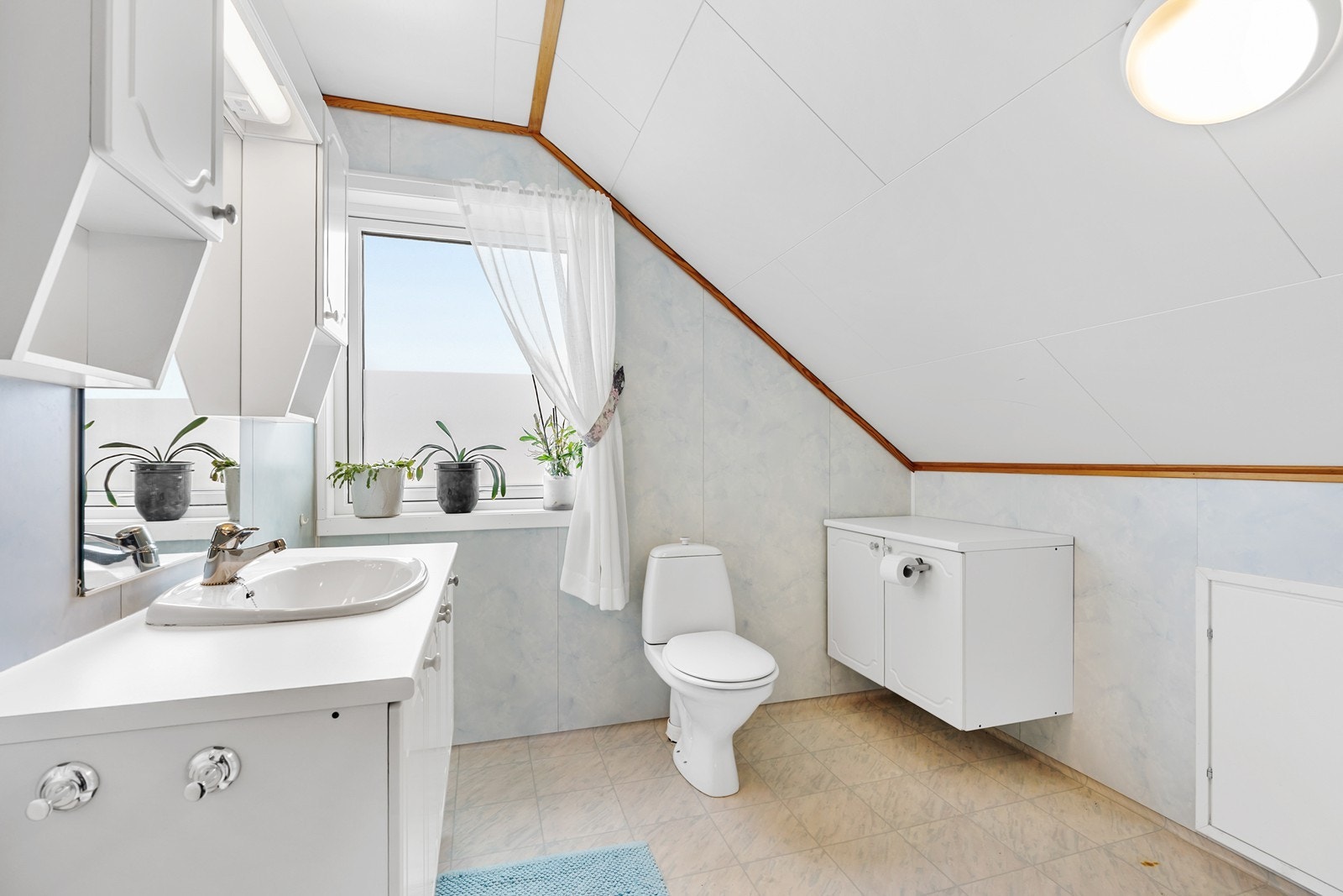 Badet på loftet er utstyrt med baderomsplater på vegger, servant med skap, og gulvbelegg. Galleribilde