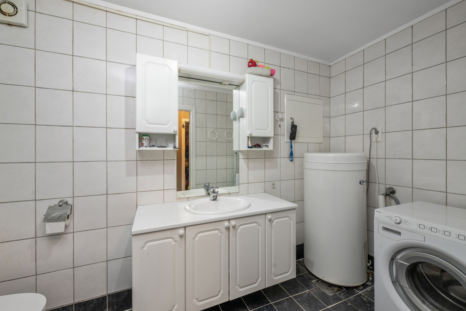 Flislagt bad med dusjkabinett og stor baderomsinnredning for lagring av baderomsartikler.
