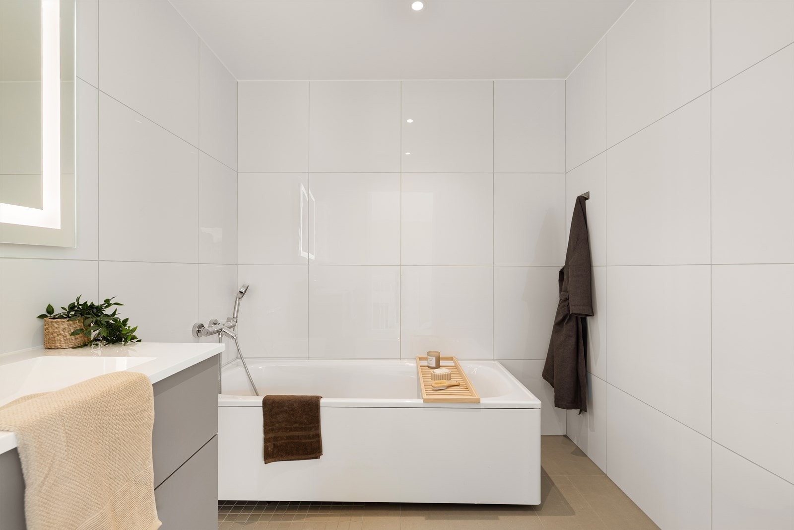 Lekkert helfliset bad med elektriske varmekabler. Badet er innredet med badekar, heldekkende servant, speil med belysning og vegghengt toalett. Galleribilde