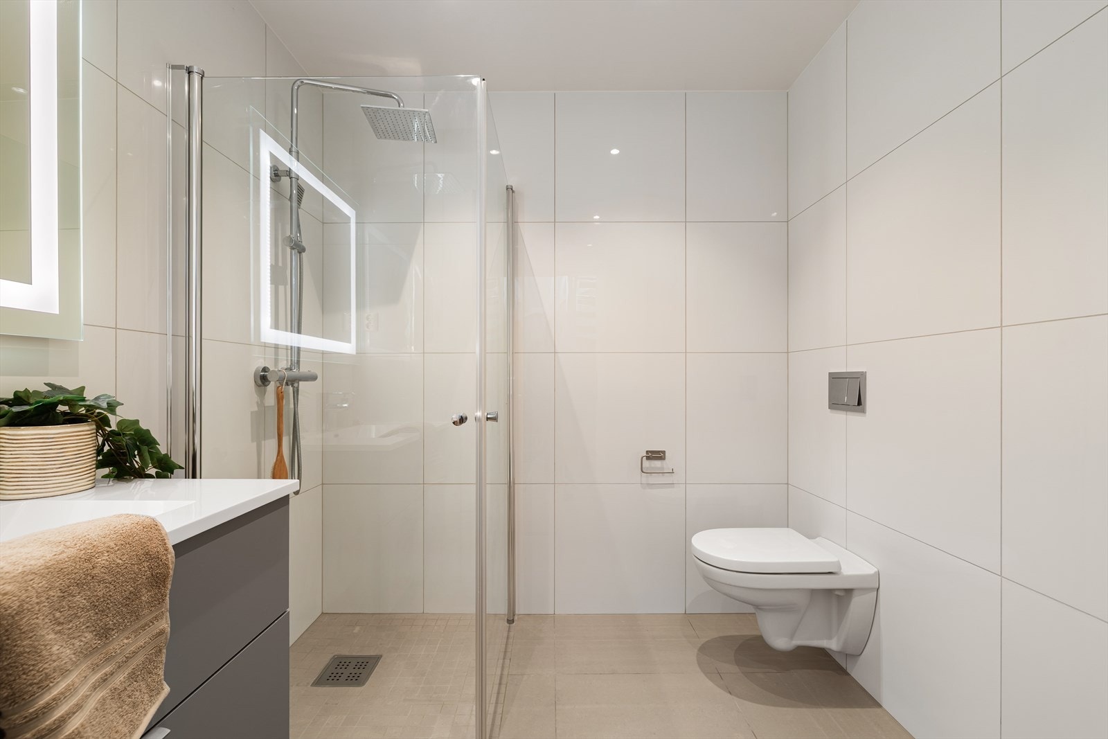 Badet i 1.etasje har baderomsmøbel med heldekkende servant, speil med belysning, vegghengt toalett og dusj med innfellbare dører i glass samt dusjgarnityr med "regnfall" og hånddusj. Galleribilde