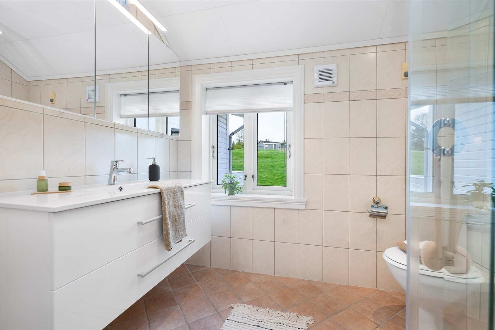 Det andre badet i etasjen er plassert mot vest. Det lyse helflisete badet har en slett, hvit og elegant baderomsinnredning med heldekkende servant, et frittstående toalett. Galleribilde