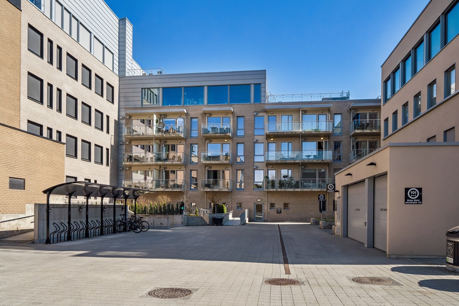 Flott bakgård med med sittegrupper, sykkelstativer, avfallshåndtering/molokker og innkjøring til parkeringskjeller. Galleribilde