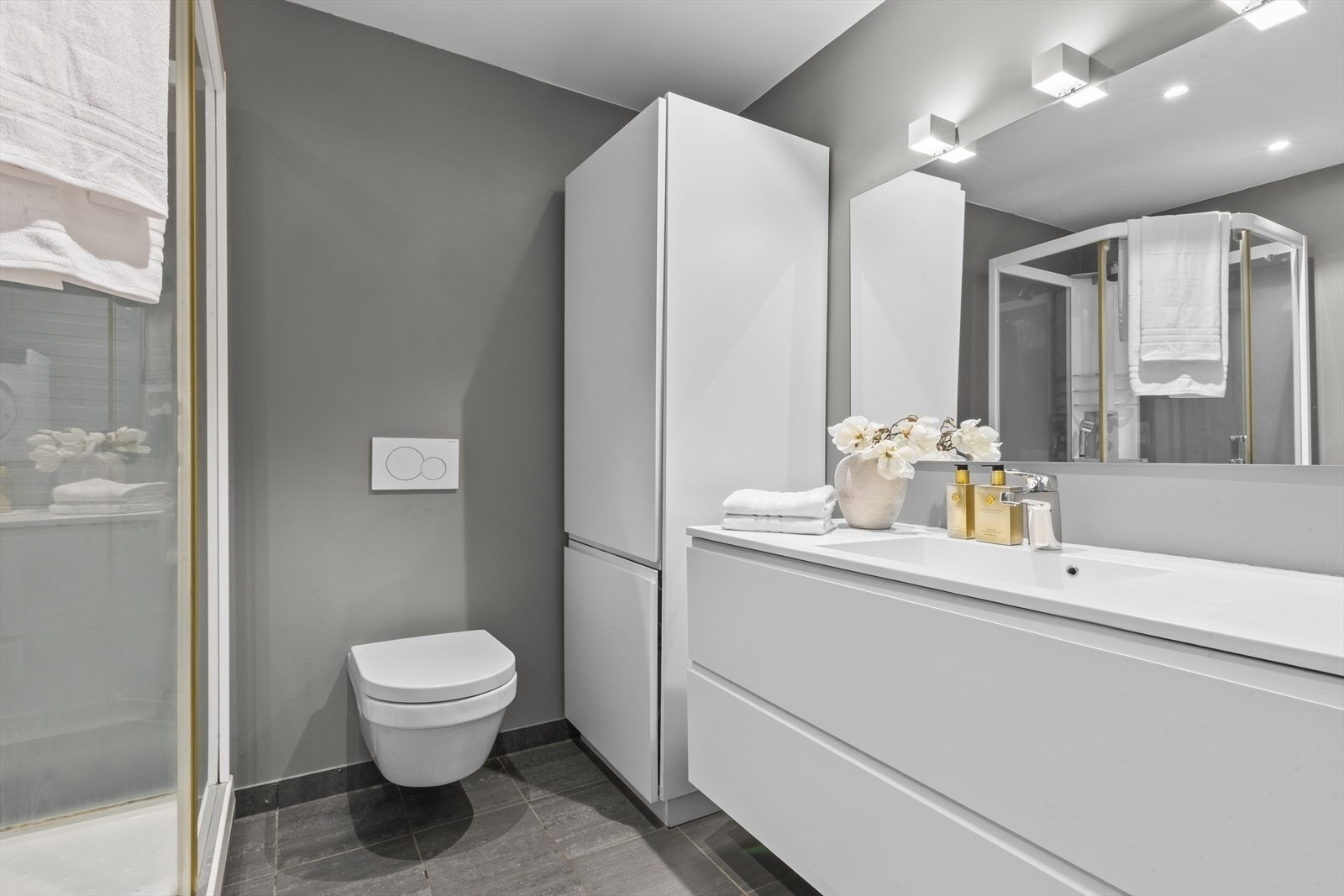 Badet har fliser på gulvet og malte vegger, med sanitærutstyr inkludert vegghengt toalett og opplegg for vaskemaskin. Galleribilde