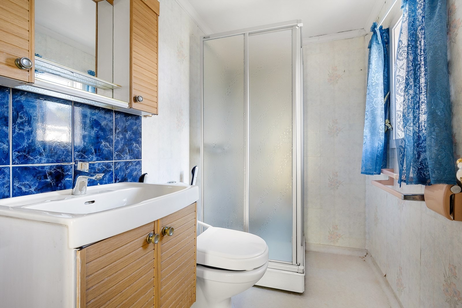 Badet er innredet med dusjkabinett, servant, baderomsmøbel og wc, og har belegg på gulv og tapet på vegger. Galleribilde