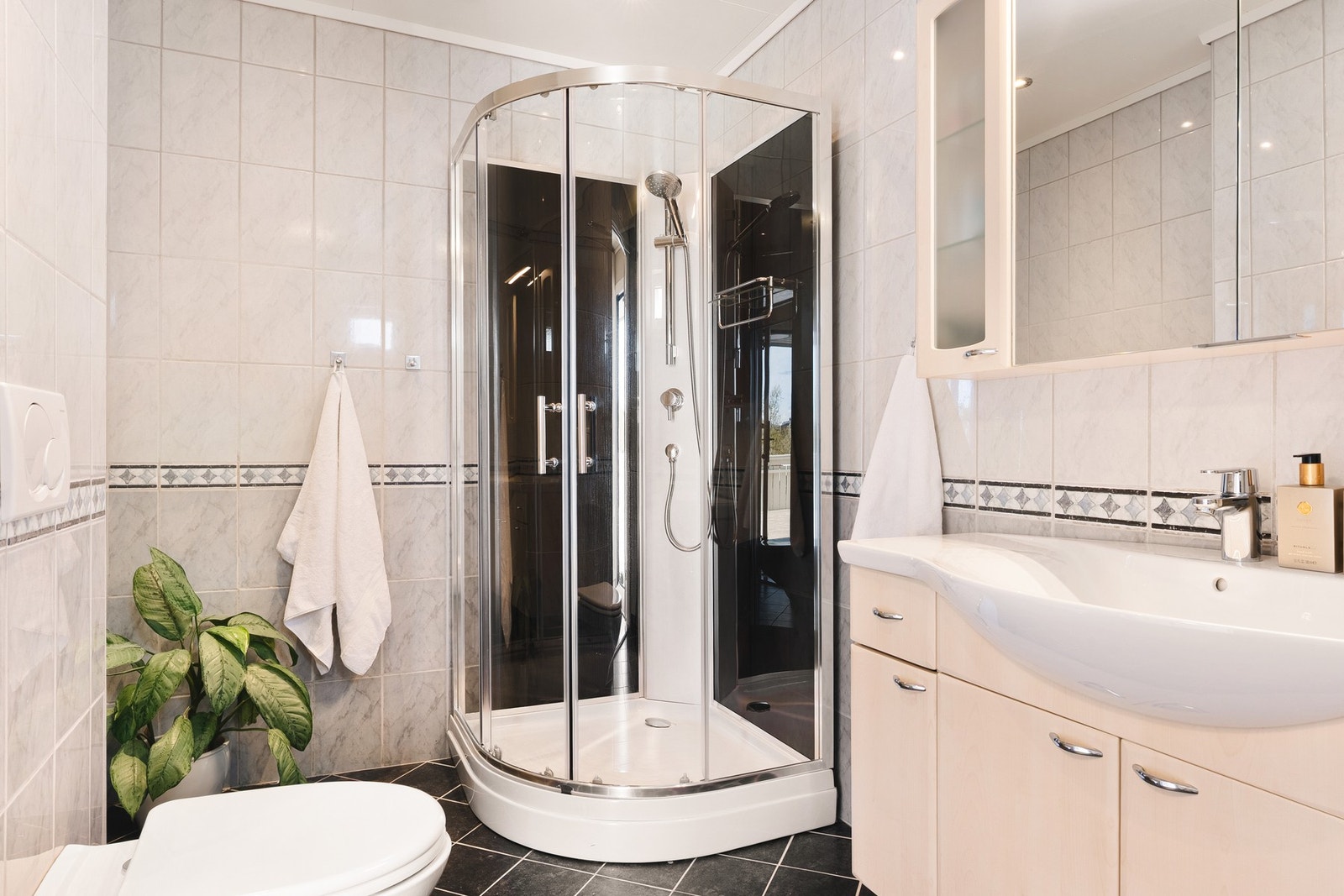 Badet er innredet med vegghengt toalett, baderomsinnredning med servant, opplegg for vaskemaskin og dusjkabinett. Galleribilde