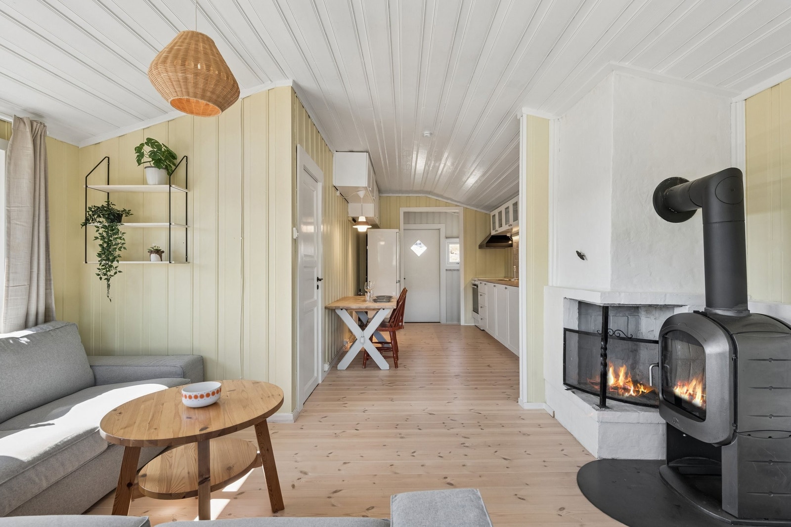 Stue: Hardvoksoljet furugulv, malt trepanel på vegger og himling. Peis og vedovn. Flammer lagt til av fotografen. Galleribilde