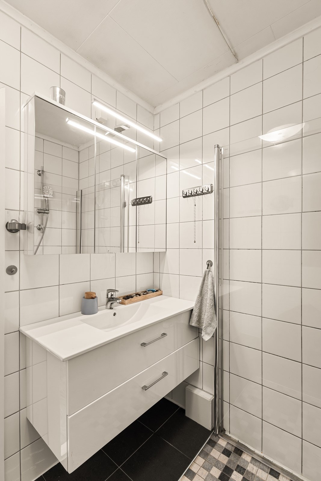 Badet er utstyrt med dusjhjørne, servant med skuffeseksjon og speilskap som gir praktisk oppbevaringsplass. Galleribilde