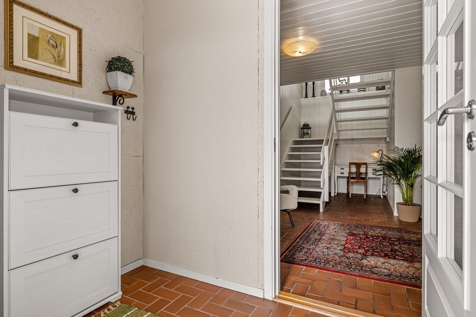 Vindfang med plass til skoskap og klesoppheng, med videre atkomst til hallen. Her er det innvendig trapp i malte trekonstruksjoner som binder de to etasjene sammen. Galleribilde