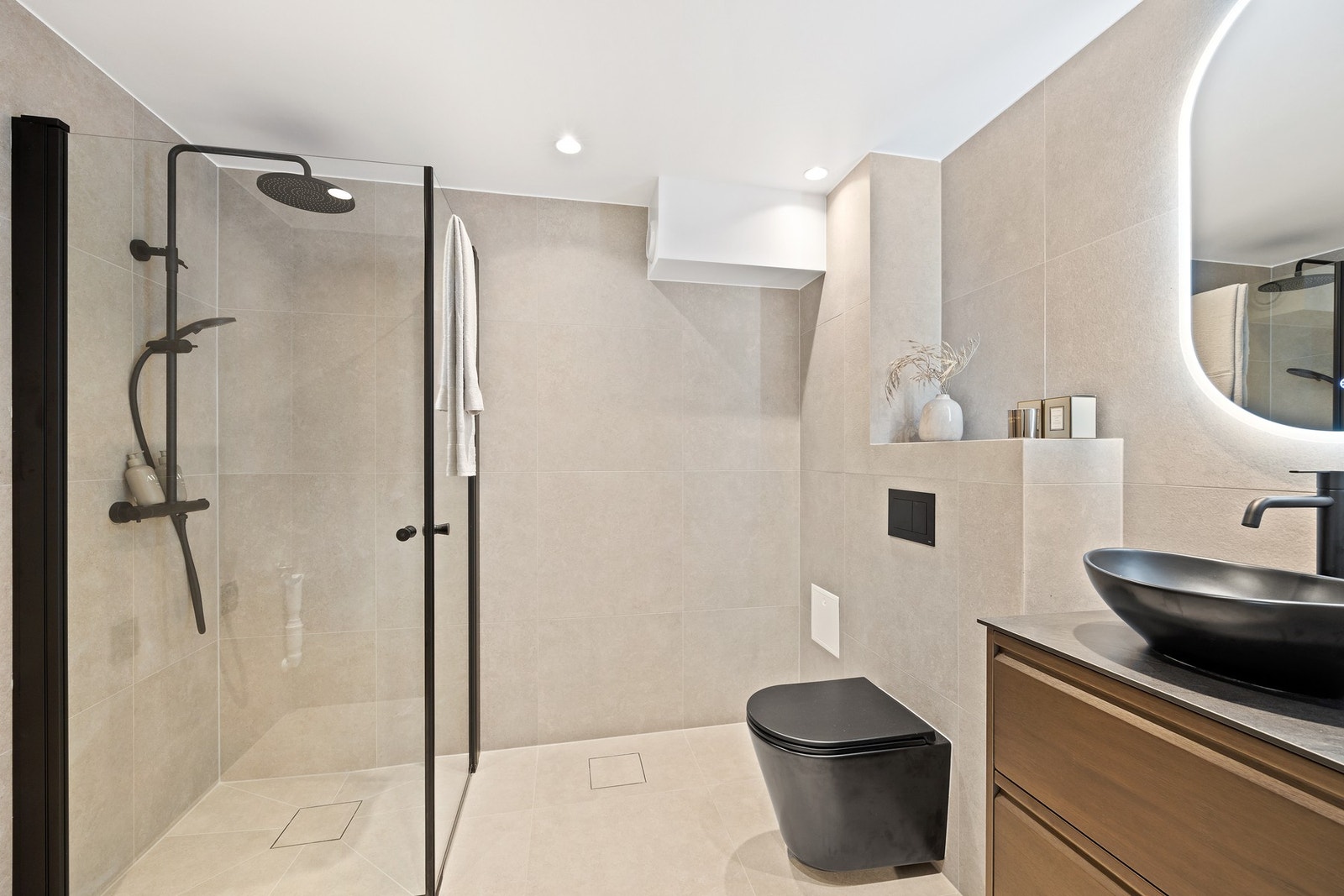 Baderom 1 med tilgang fra entréen er lekkert og delikat med moderne finish. Vegghengt wc, dusjhjørne, servantmøbler med toppmontert vask, speil med belysning og opplegg for tørke-/vaskemaskin. Galleribilde