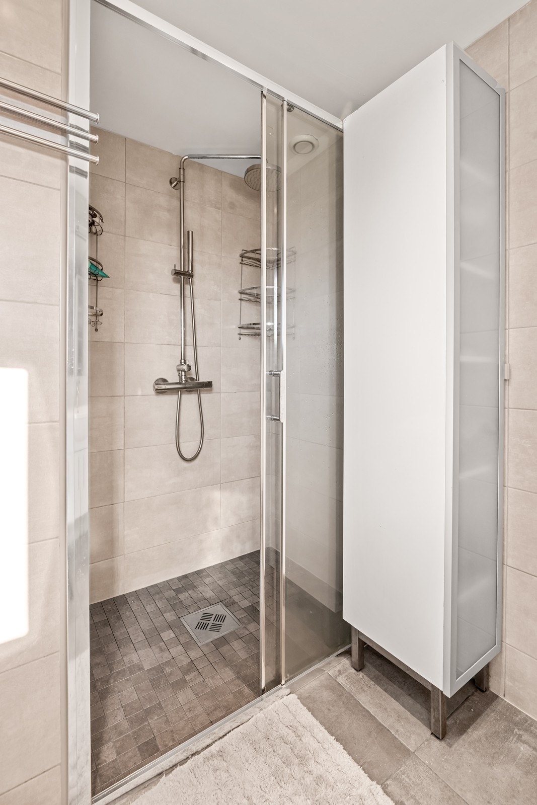 Badet har flislagte gulv og vegger, elektriske varmekabler og en dusjløsning med glassvegger. Galleribilde