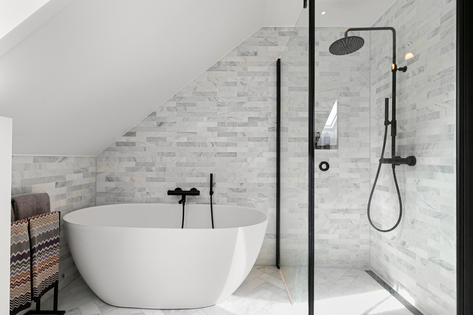 Delikate marmorfliser kombinert med sorte detaljer og gode lysforhold fra takvindu gir badet et eksklusivt uttrykk. Galleribilde