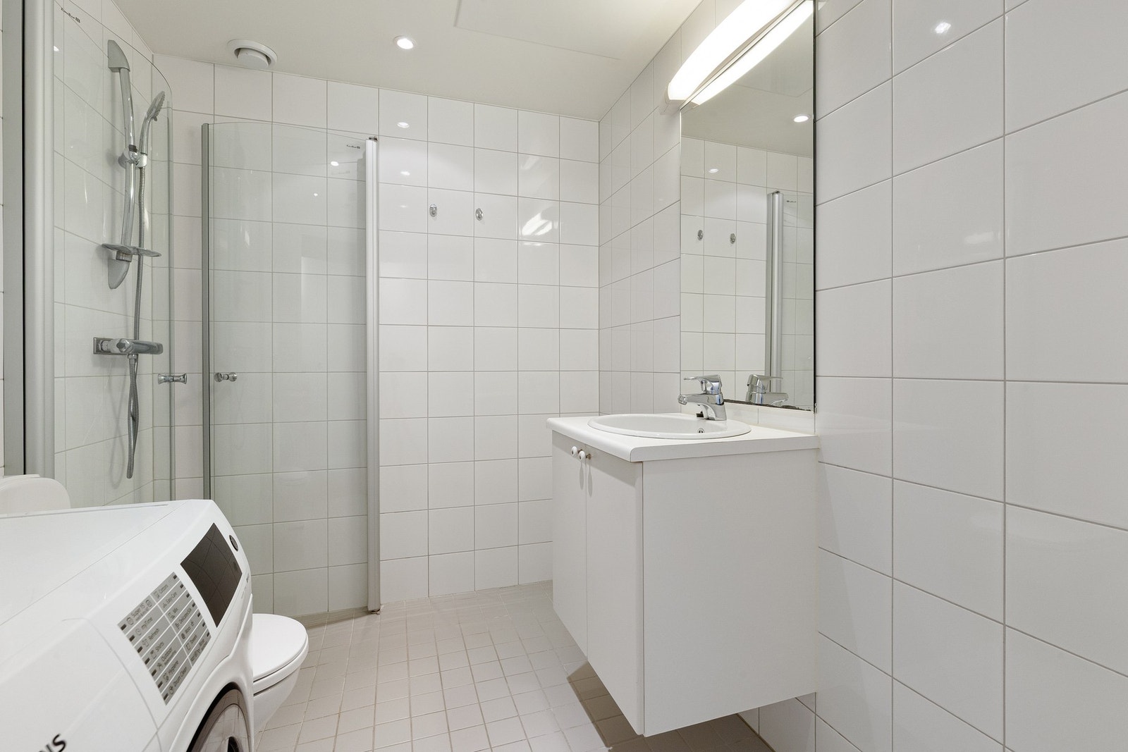 Innredningen består av servantinnredning, speil på vegg over servant, vegghengt toalett, dusjhjørne med svingbare glassdører og opplegg for vaskemaskin. Galleribilde