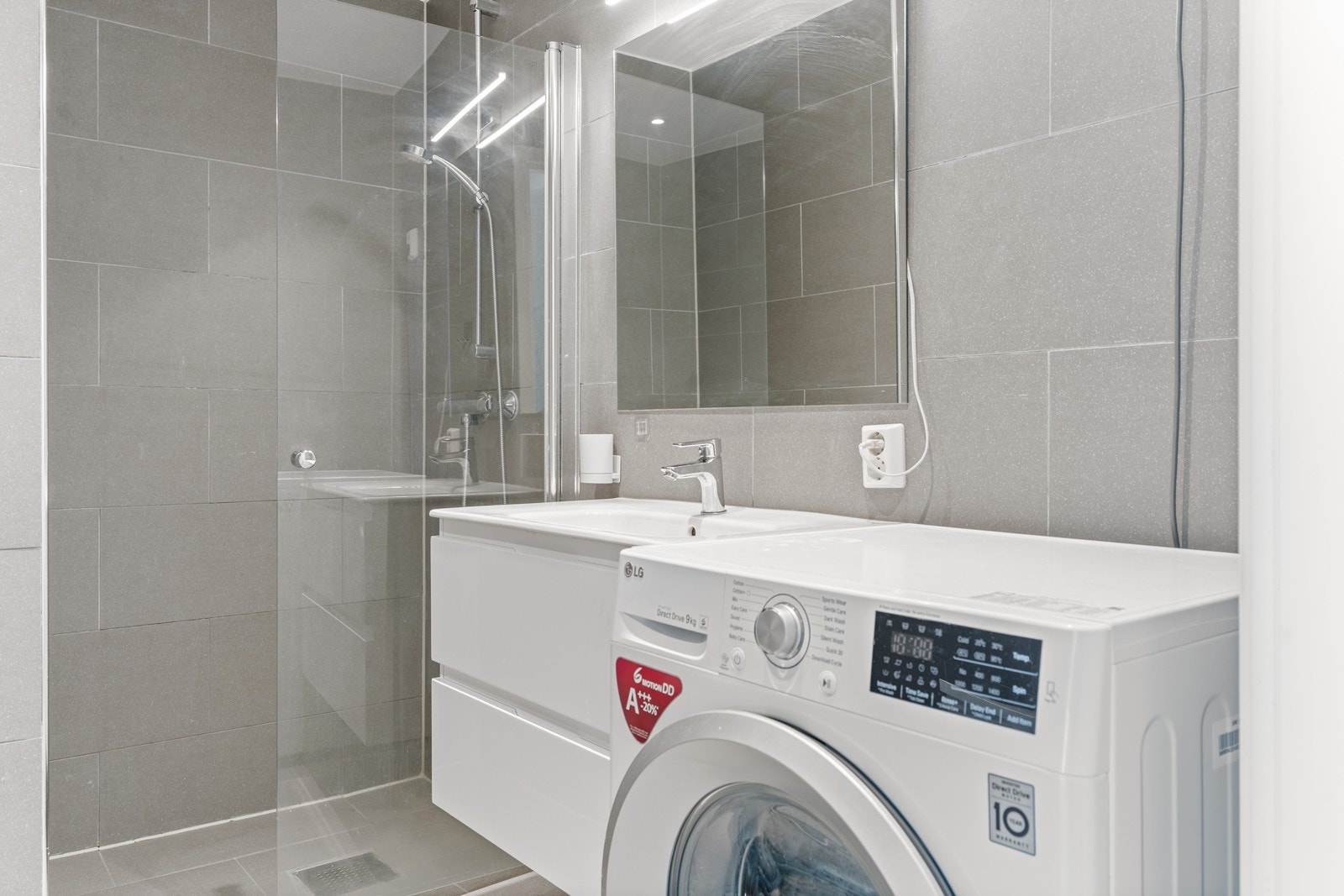 Badet/vaskerommet er innredet med hvit baderomsinnredning, vegghengt toalett og dusjnisje med glassvegg, samt opplegg for vaskemaskin (vaskemaskinen medfølger i handelen) Galleribilde