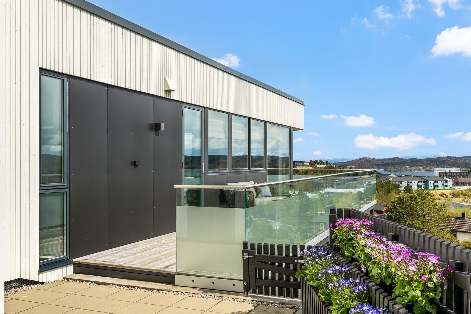 Utearealet er oppdelt i flere spennende soner og du får både veranda med glassrekkverk, inngjerdet hage og dette hyggelige hjørnet, med beleggingssten og plassbygdeblomsterkasser. Galleribilde