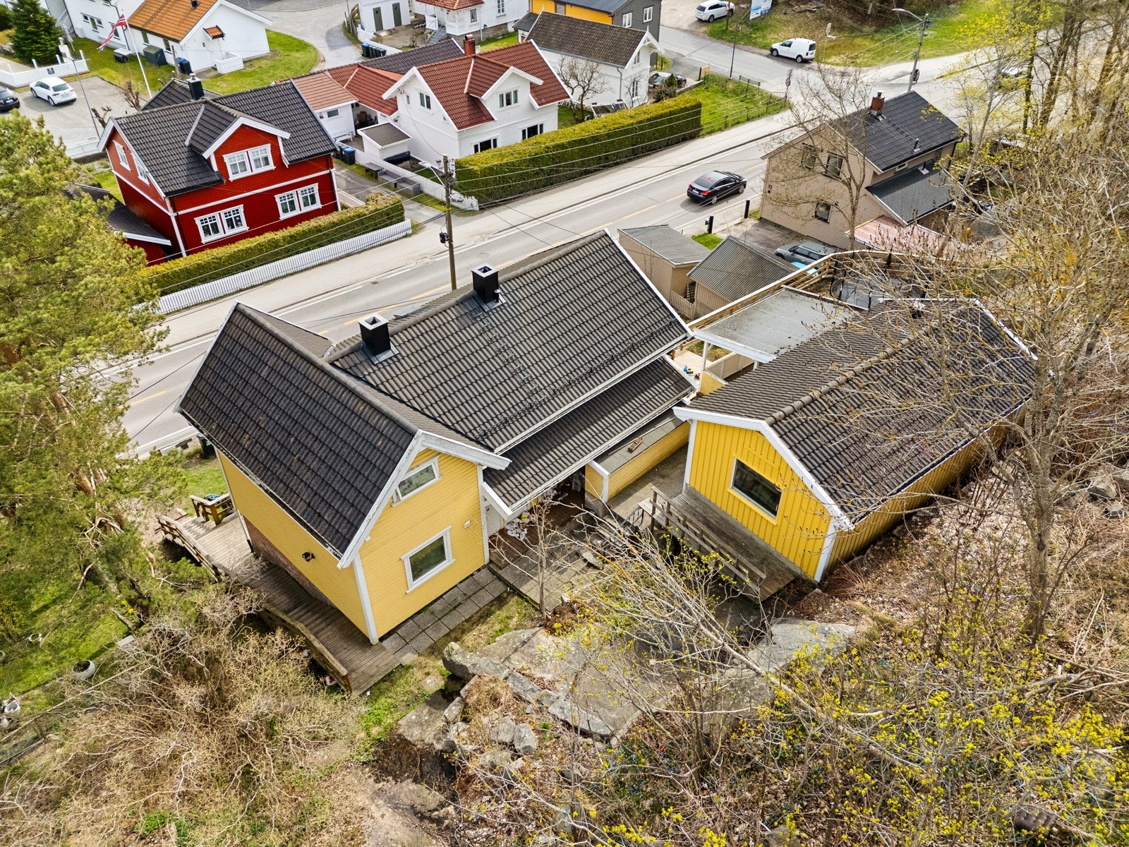 Eneboligen ligger på en skrånende tomt, opparbeidet med noe gressplen og diverse beplantning. Rett utenfor døra er det en bussholdeplass. Galleribilde