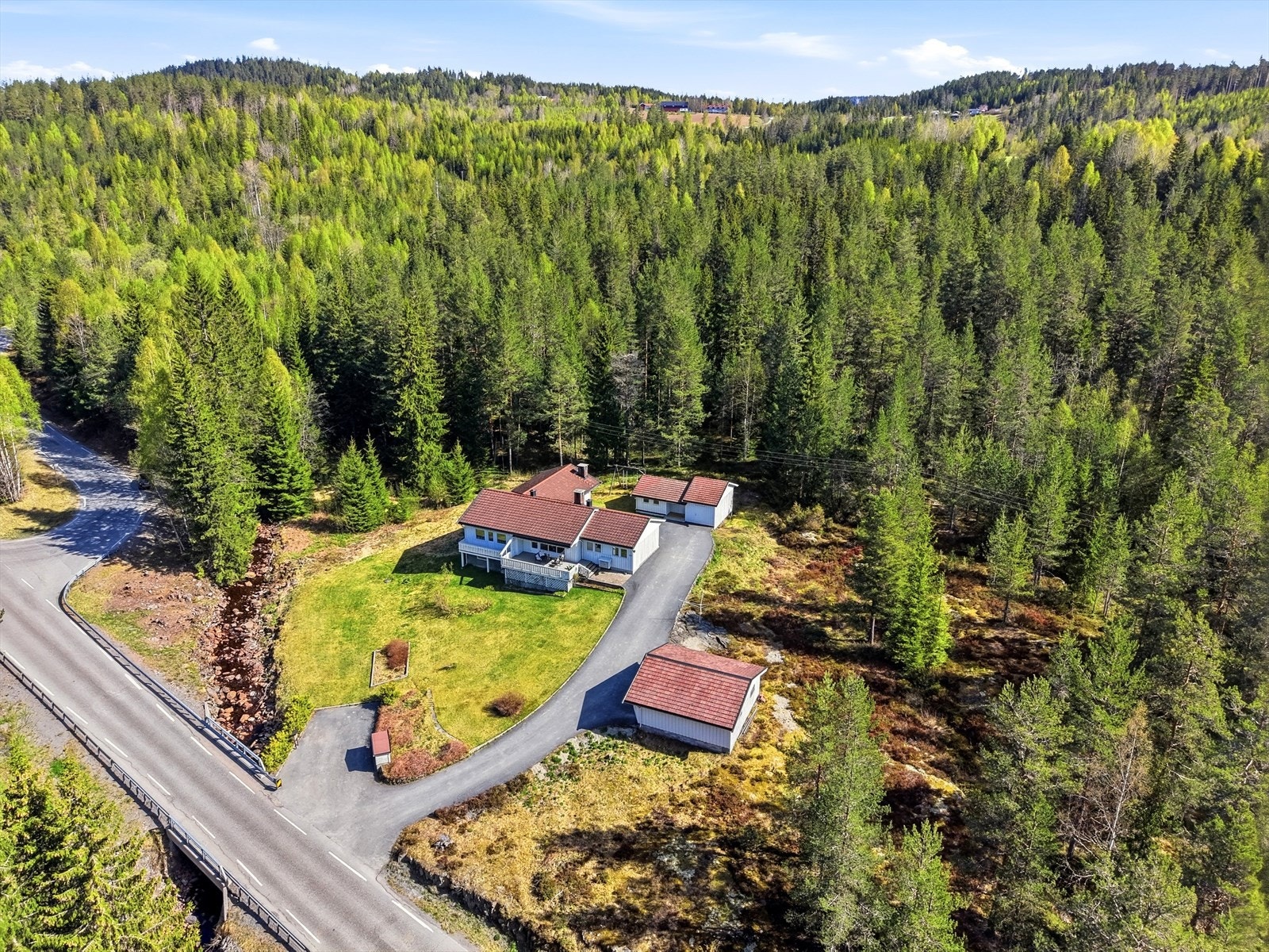 Eiendommen ligger skjermet til på en kupert tomt med asfaltert gårdsplass, dobbelgarasje og en separat sidebygning for lagring. Galleribilde