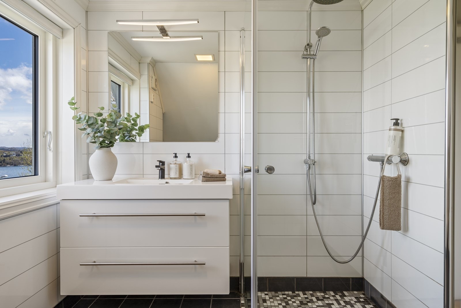 Badet er utstyrt med dusjnisje med svingbare glassdører, vegghengt toalett og en seksjon med vask. Galleribilde