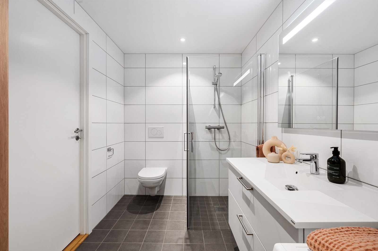 Badet på 5,6 m² holder en moderne og helhetlig standard med keramiske fliser på både gulv og vegger, og en himling med innfelte spotter som gir et behagelig lys. Galleribilde