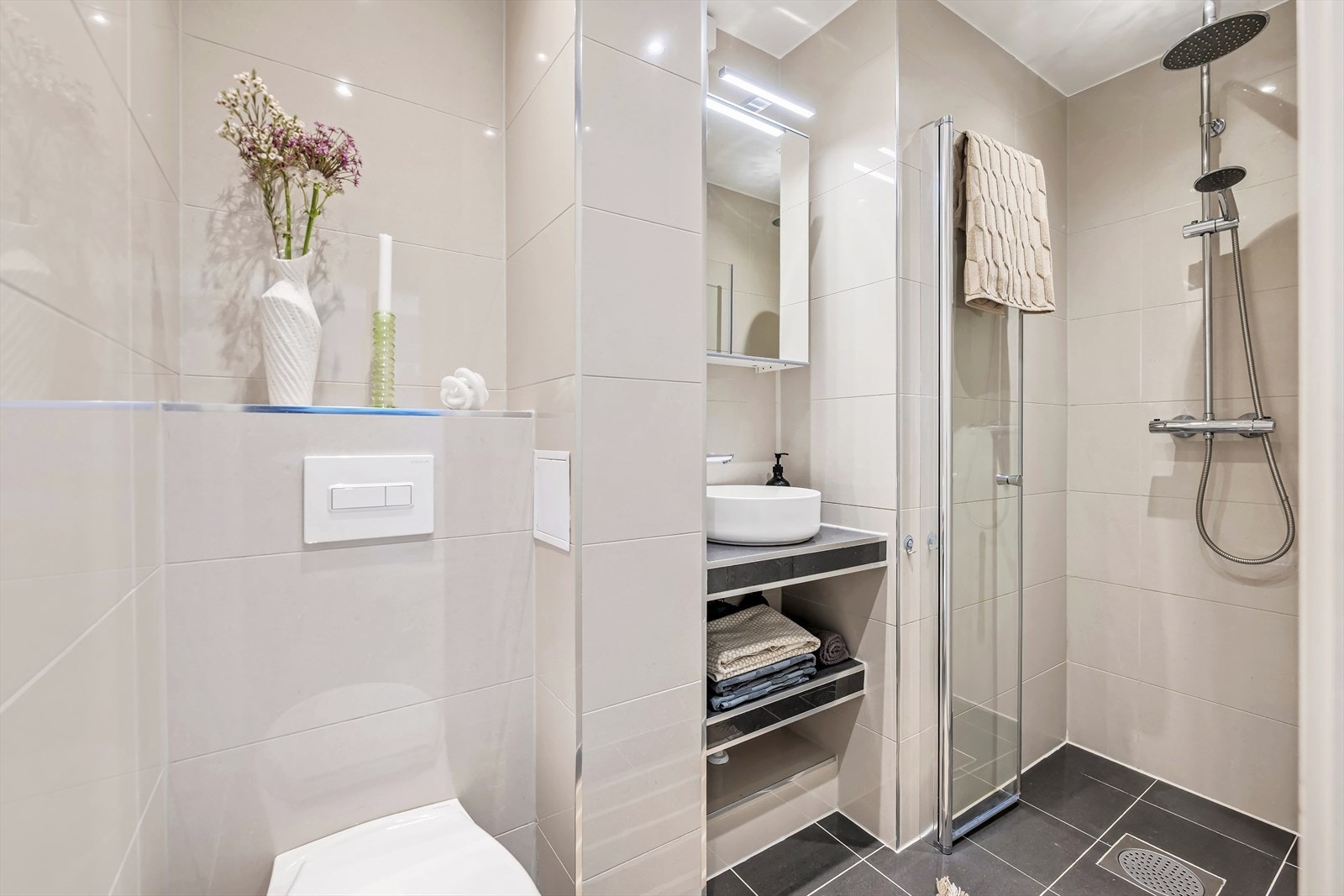 Delikat flislagt bad med integrert himlingsbelysning og varmekabler i gulvet. Badet består av bolle-servant på plassbygd innredning, speilskap med lysarmatur, veggmontert klosett og dusjnisje. Galleribilde
