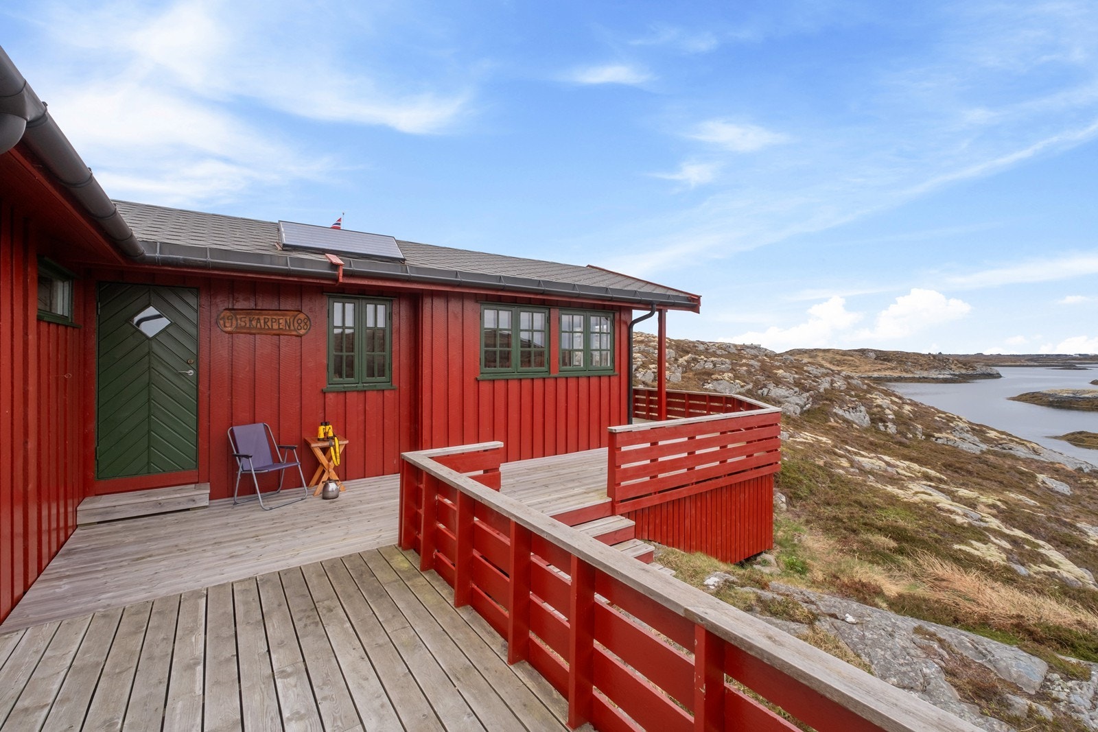 Hytta har en markterrasse med spaltedekke i tre og rekkverk, fundamentert på støpte søyler. Solcellepanel på taket. Galleribilde
