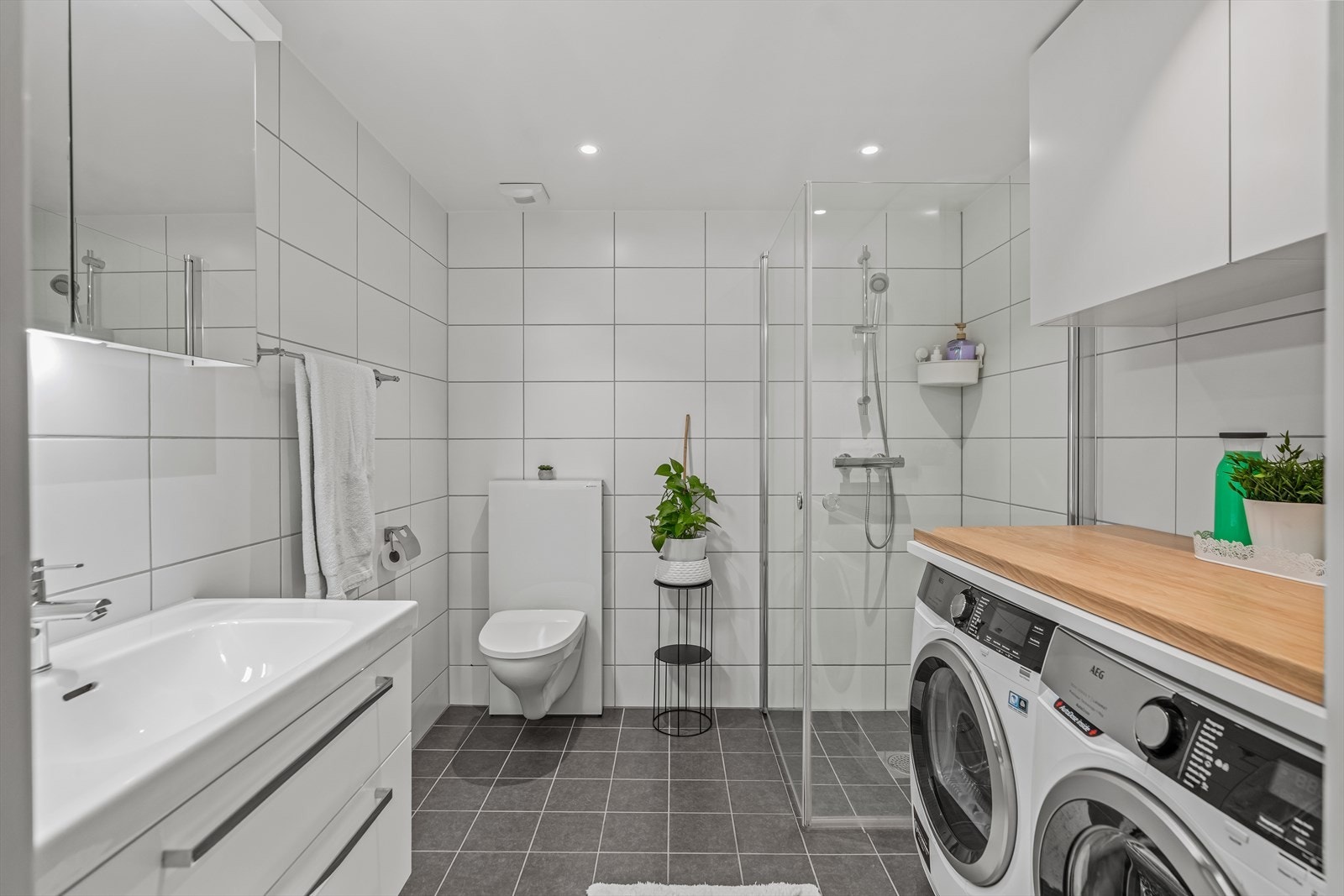 Badet inneholder speilinnredning med lys, vegghengt toalett og dusj i hjørne bak svingbare glassvegger. Galleribilde
