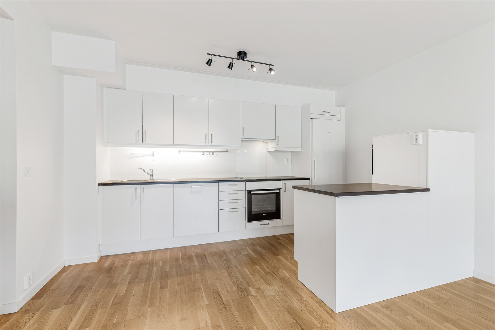 Kjøkken med innredning fra byggeåret. Innredningen har glatte fronter og benkeplater av laminat. Belysning under overskapene.
Foto: Trond Reder Galleribilde