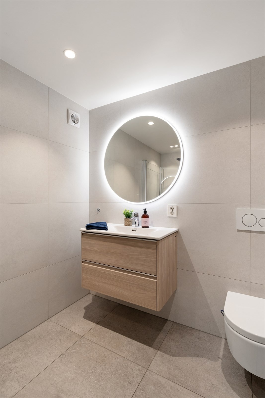 Badet er innredet med baderomsinnredning med servant, speil med integrert belysning, dusjhjørne med glassdører og vegghengt toalett. Galleribilde