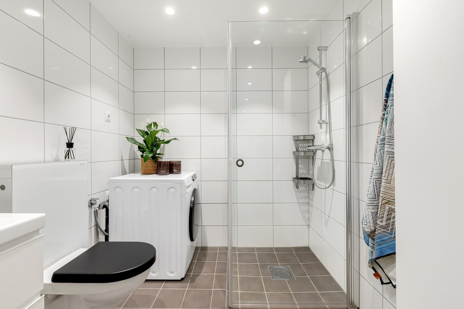 Badet er utstyrt med veggmontert toalett fra Geberit, dusjhjørne med innfellbare glassdører og baderomsmøbel med skuffer, servant med ettgrepsbatteri og speil. Galleribilde