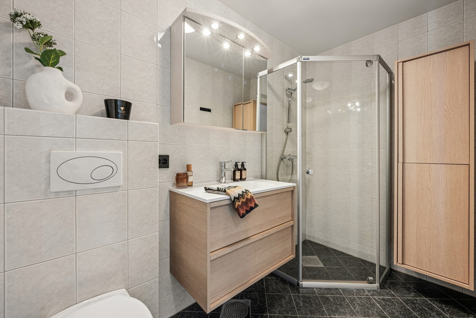 Badet er utstyrt med dusjhjørne med innfellbare dører, vegghengt toalett og mekanisk avtrekk. Galleribilde