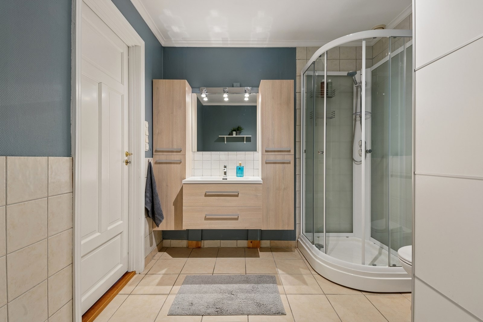 Badet har flislagt gulv med varmekabler, delvis flislagte vegger, dusjkabinett og vegghengt toalett. Galleribilde