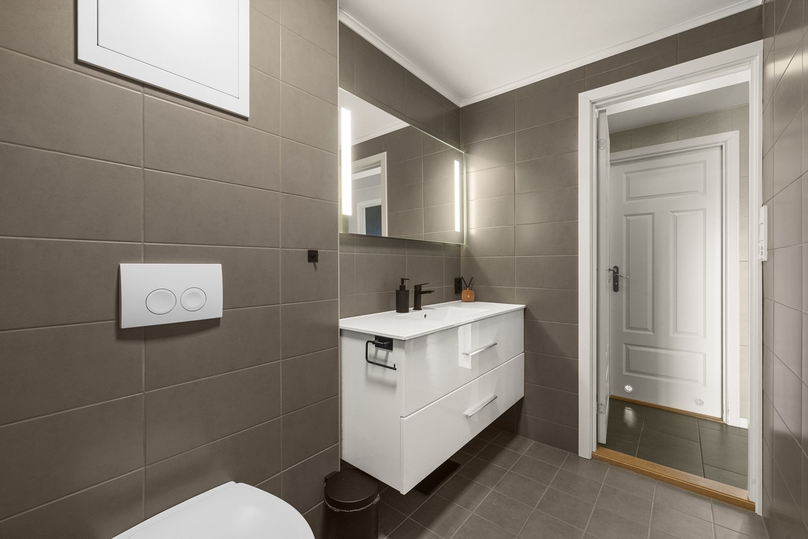 Pen og tidløs innredning med skuffer og heldekkende servant. På vegg over servant er det montert speil med belysning. Badet har balansert ventilasjon. Galleribilde