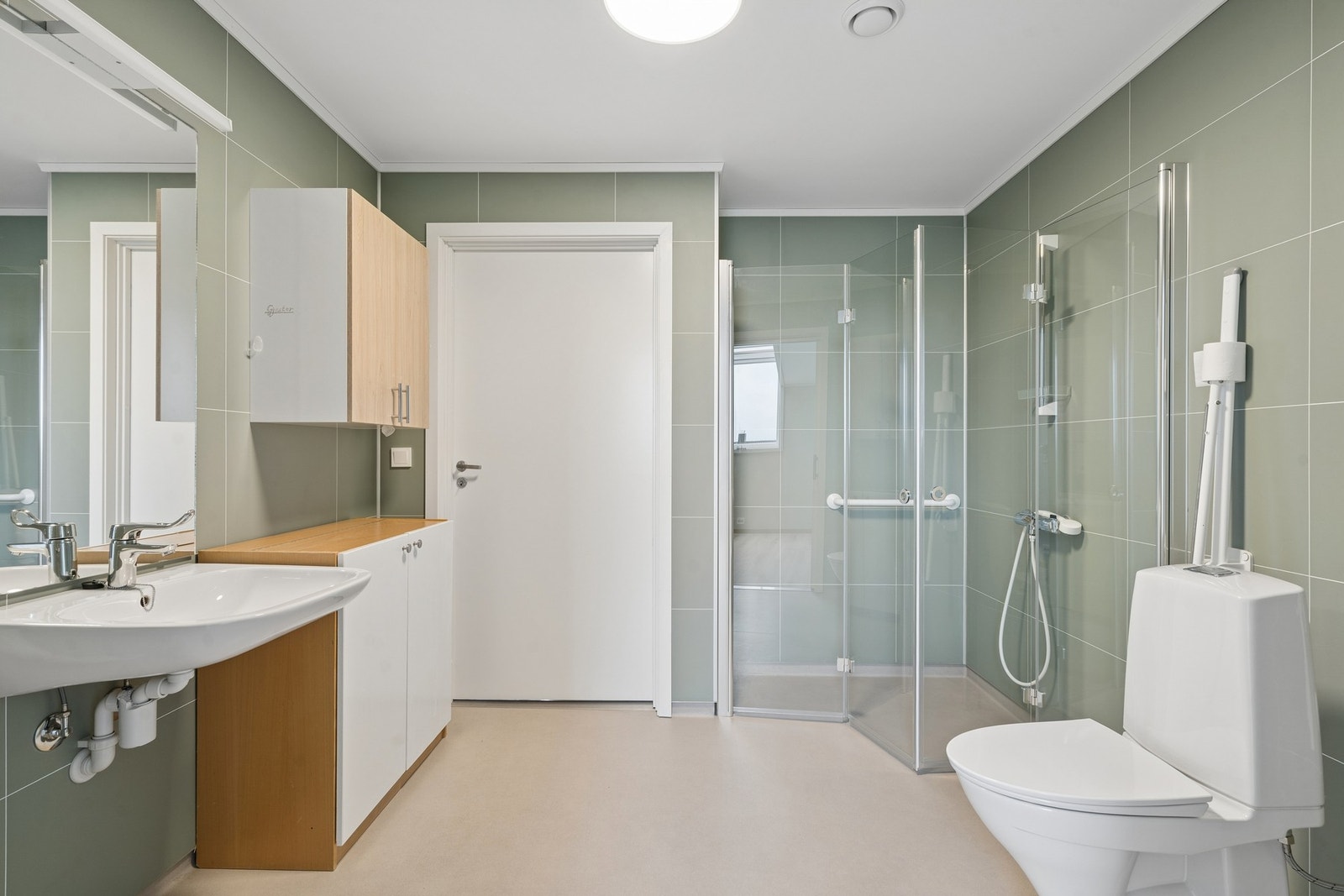 Badet er innredet med servant, toalett, dusjhjørne med innfellbare glassdører, og opplegg for vaskemaskin. Galleribilde