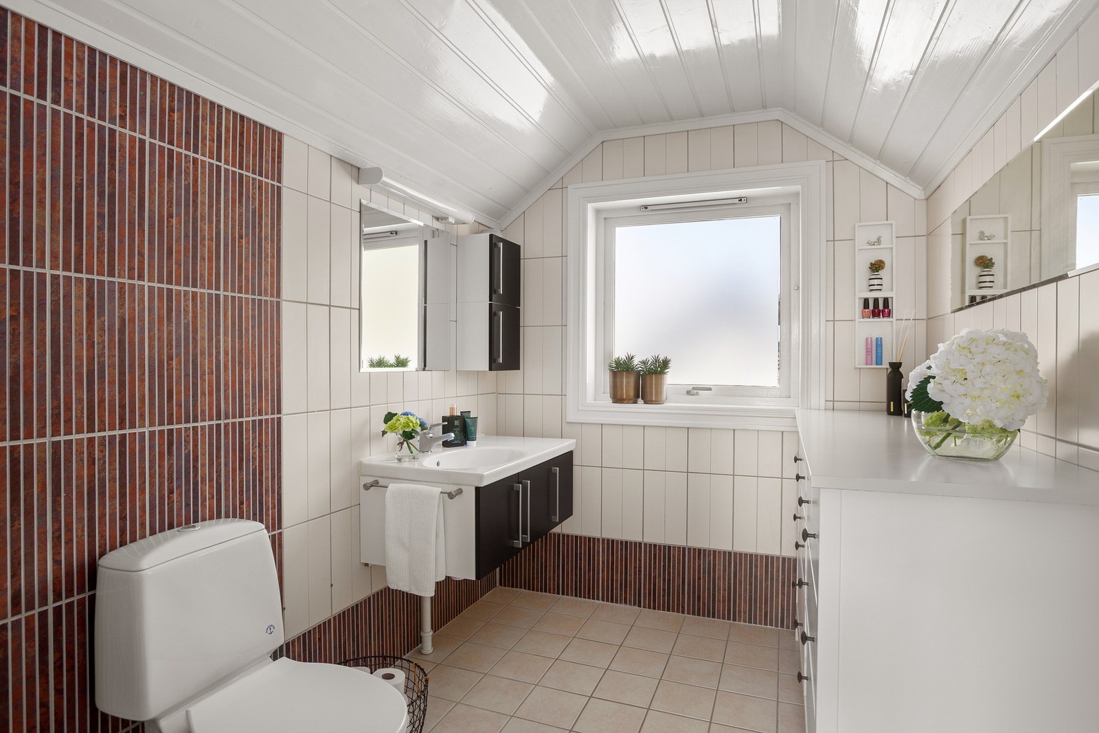 Badet er innredet med gulvstående toalett, dusjnisje med dør i herdet glass samt vegghengt baderomsmøblement med skap, heldekkende servant og to veggskap. Galleribilde