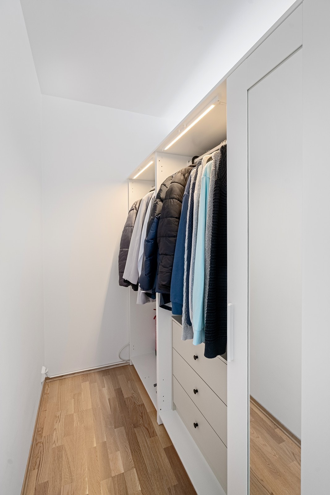 Walk-in garderobe fra soverommet med integrert belysning gir effektiv oppbevaring . Galleribilde