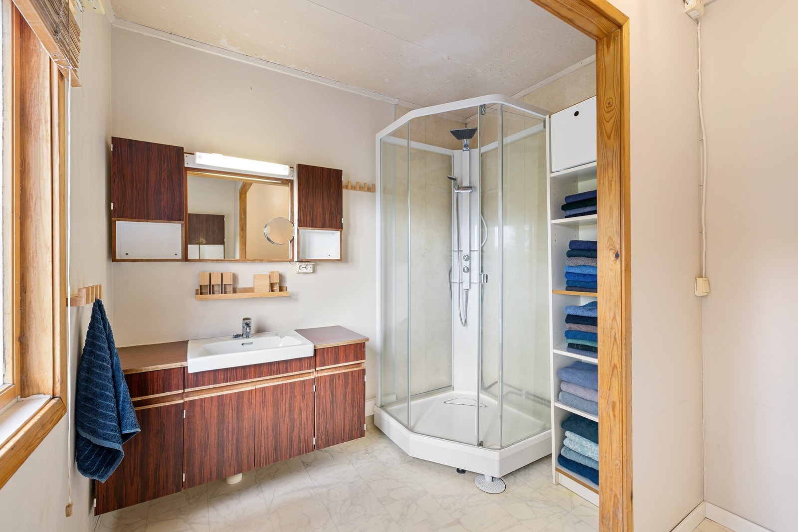 Badet har belegg på gulv og baderomsplater på vegger. Innredningen består av et underskap/overskap, servant, speil og armatur, stikk og ett dusjkabinett. Galleribilde