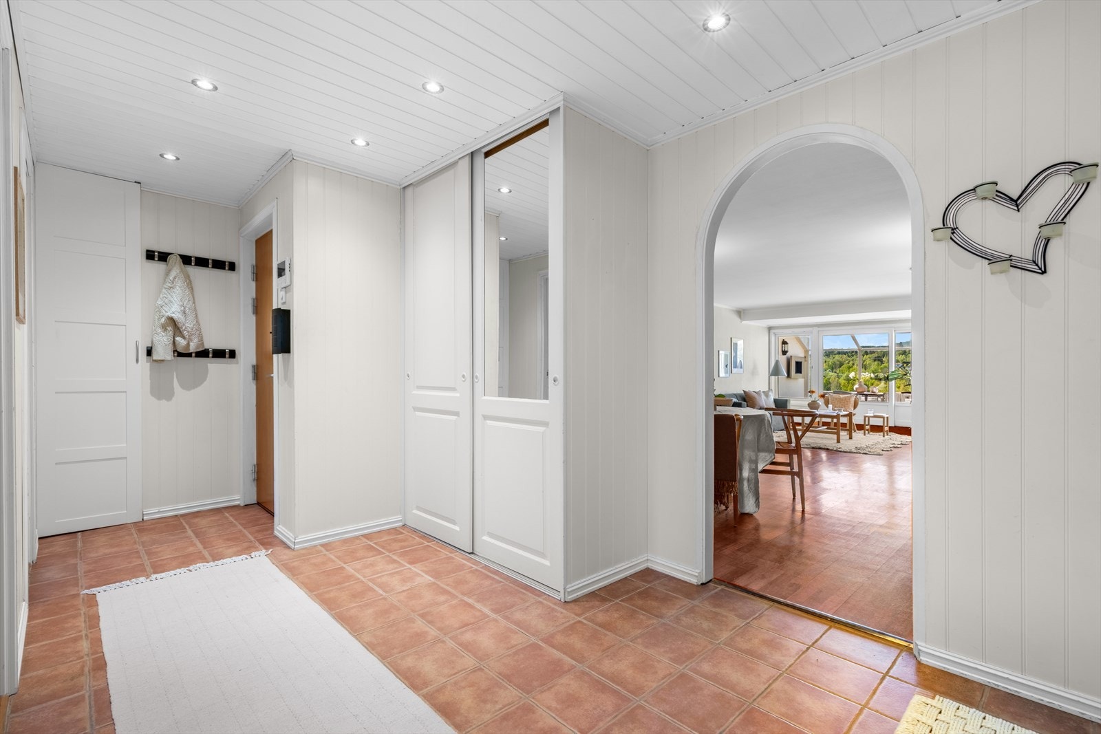 Lys og romslig entré med fliser på gulv og downlights i himling. Det er skyvedørsgarderobe for oppbevaring av klær og sko. Galleribilde