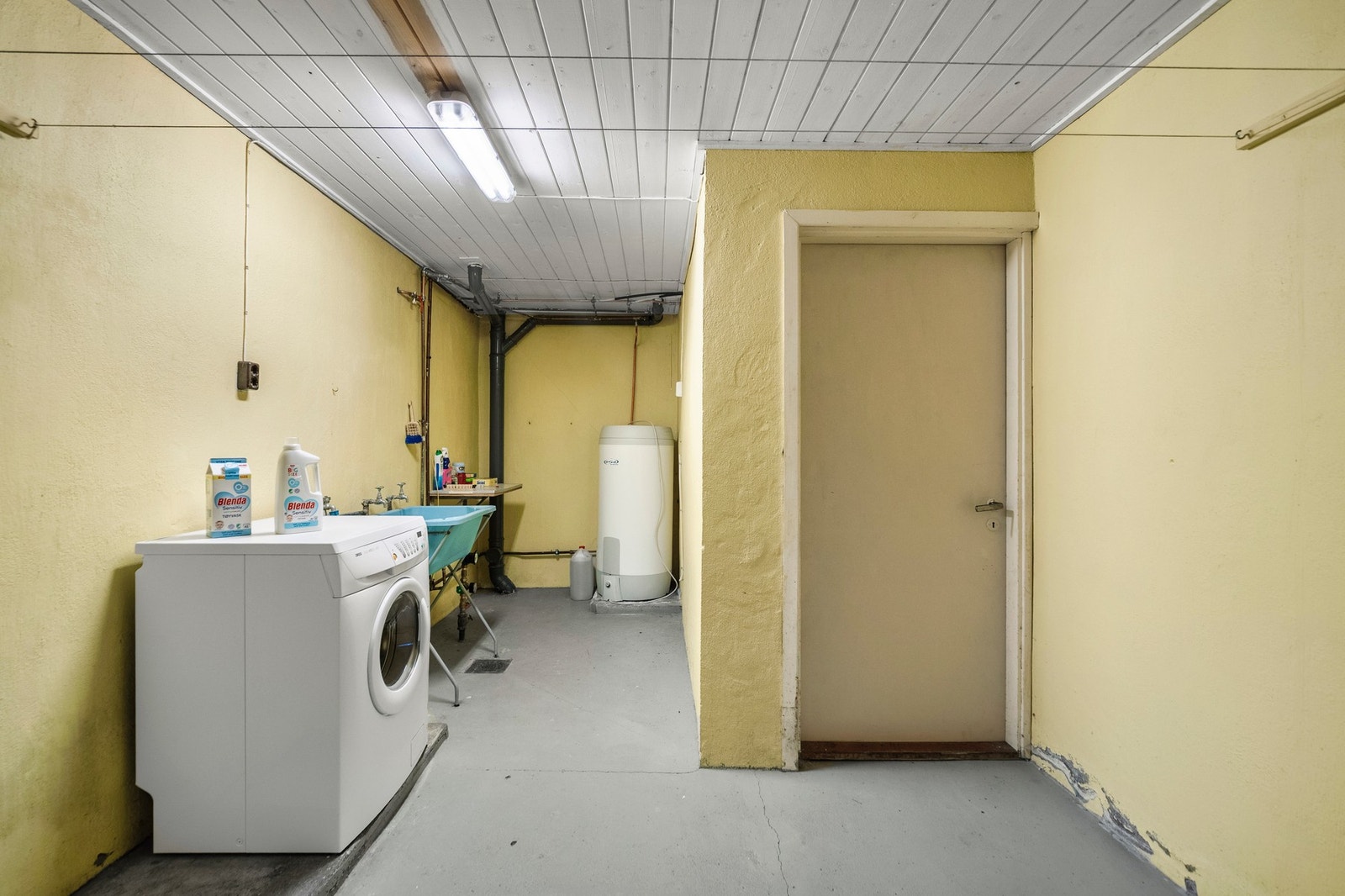 Vaskerom med malt muroverflate på gulv, malte flater på vegger og panelbord i himling. Gulvstående utslagsvask og opplegg for vaskemaskin. Galleribilde