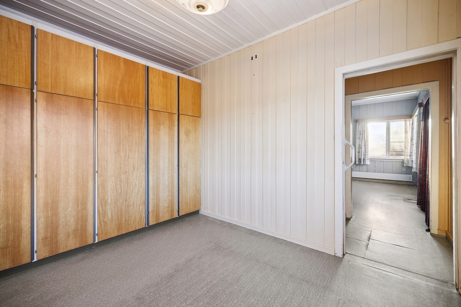 Soverom i første etasje med plassbygde garderobeskap og malt trepanel. Galleribilde