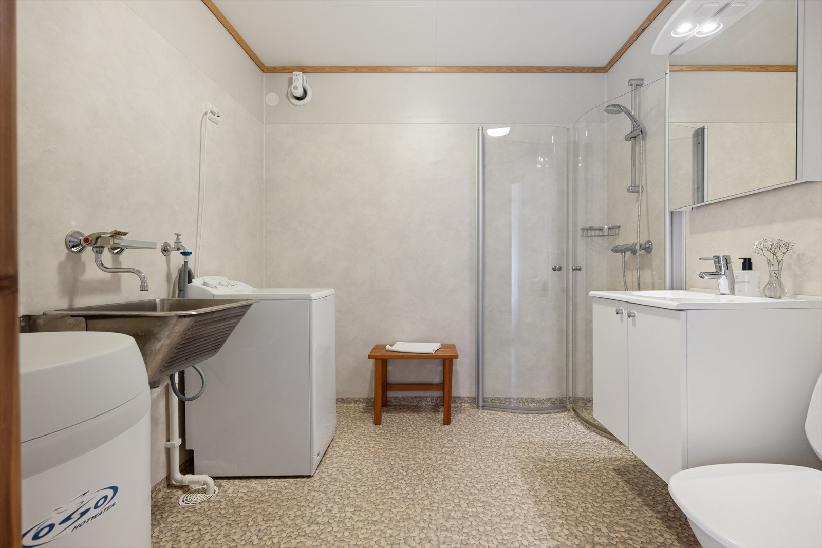 Badet er fra 2008 og er en kombinert løsning med bad og vaskerom. Det har vinyl på gulvet med varmekabler, dusjhjørne, toalett, servant og opplegg for vaskemaskin. Elektrisk styrt vifte og luftespalte under døren. Galleribilde