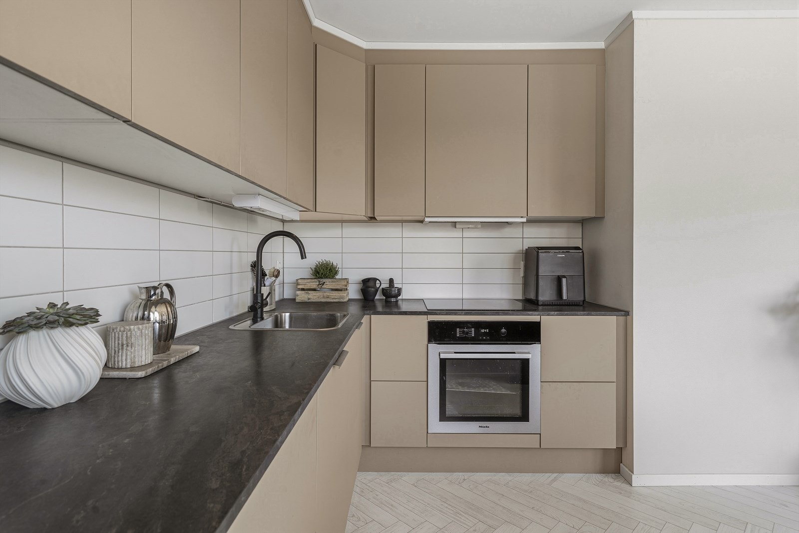 Innredningen har slette, malte fronter og laminert benkeplate med nedfelt vask og platetopp. Den mekaniske ventilatoren har avtrekk ut. Galleribilde