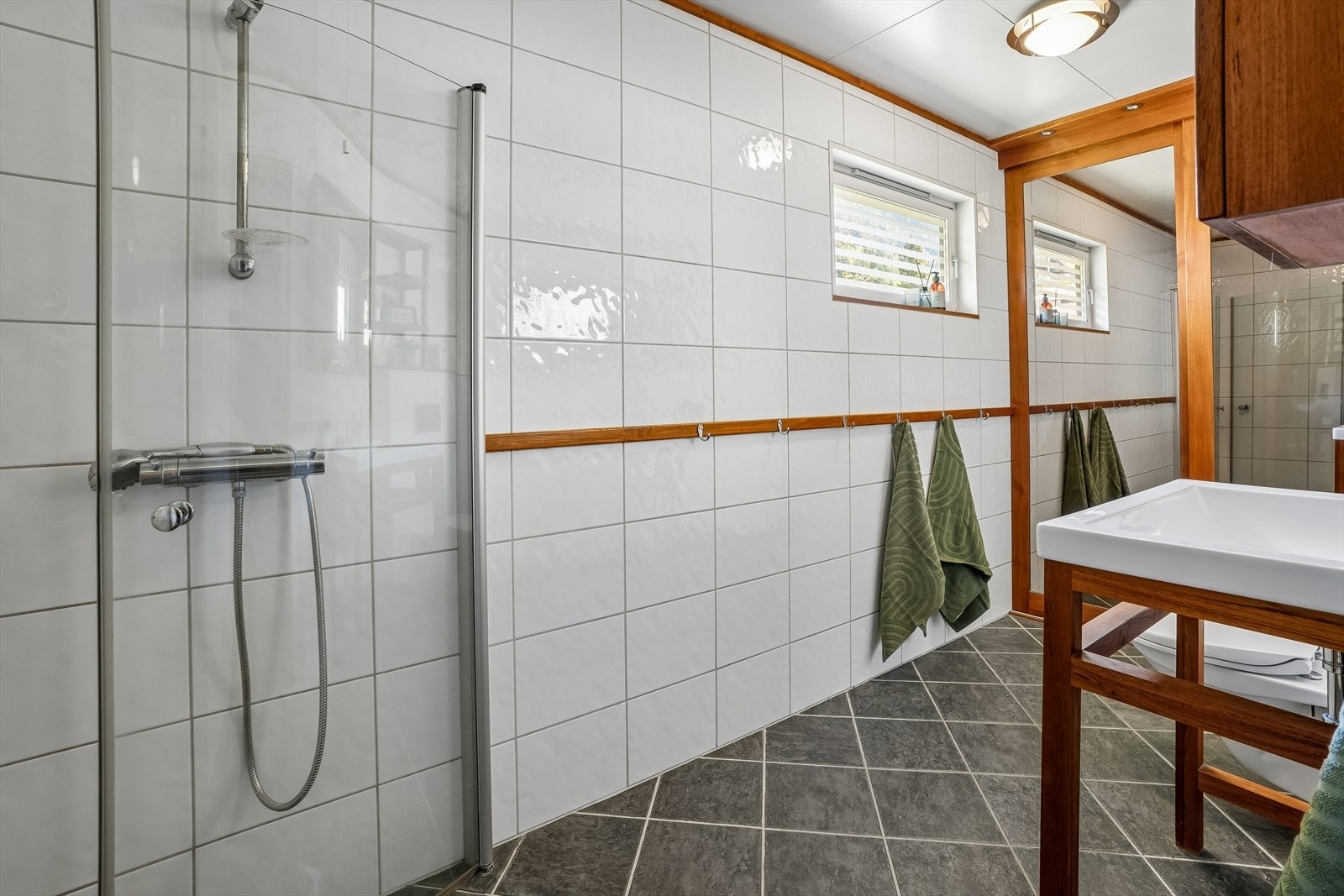 Badet i første etasje har flislagt golv med varmekablar og dusj med hengsla glasdører. Galleribilde
