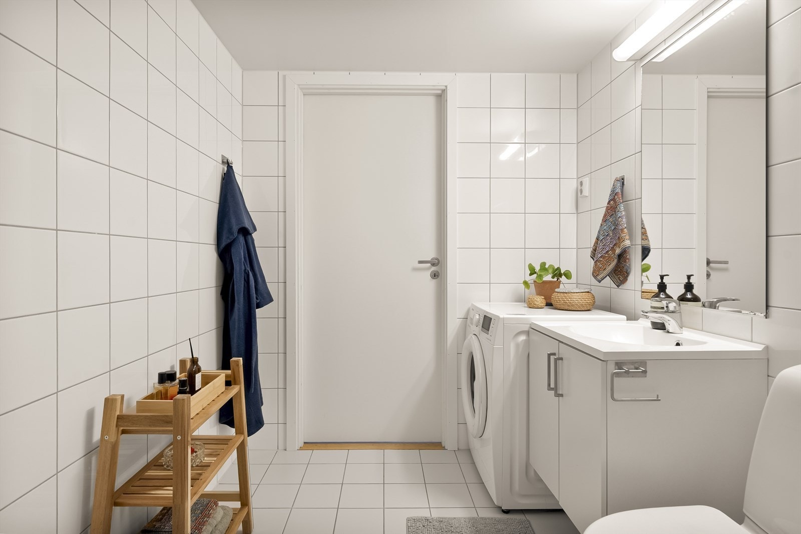 Rommet er innredet med gulvstående toalett, servantinnredning, dusjhjørne med glassdører og opplegg til vaskemaskin. Galleribilde