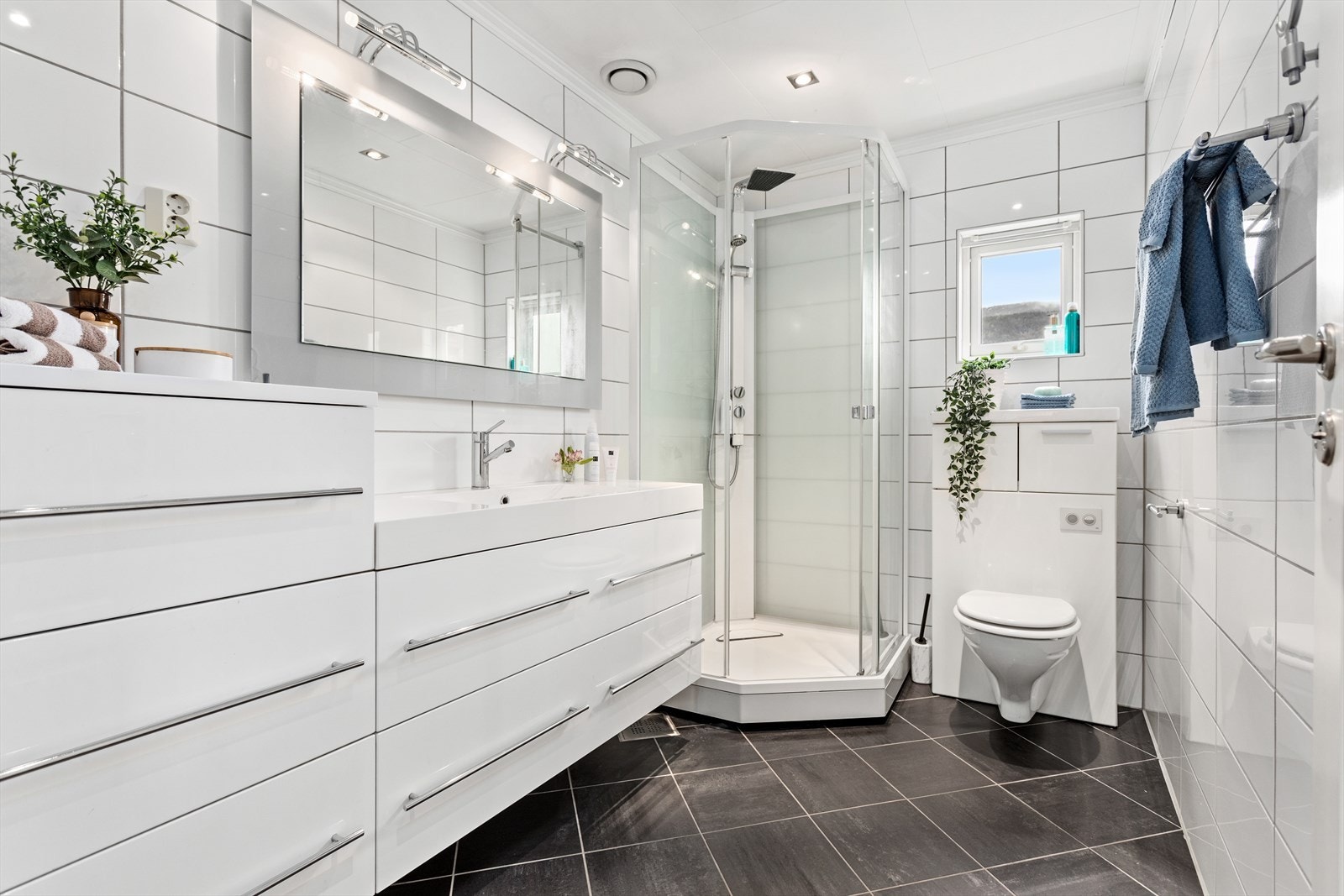 Badet i 1. etg har ei tidlaus innreiing og er utstyrt med baderomsmøbel med vask, vegghengt toalett, spegel med lys og tett dusjkabinett. Det er flis på golv og veggar. Galleribilde