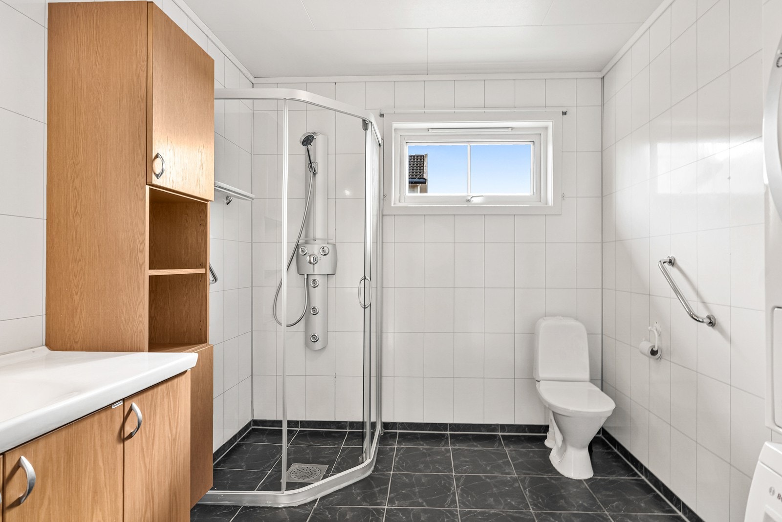 Flislagt bad med dusjhjørne, gulvmontert toalett og opplegg for vaskemaskin. Badet er oppgradert for ca 15 år siden. Galleribilde