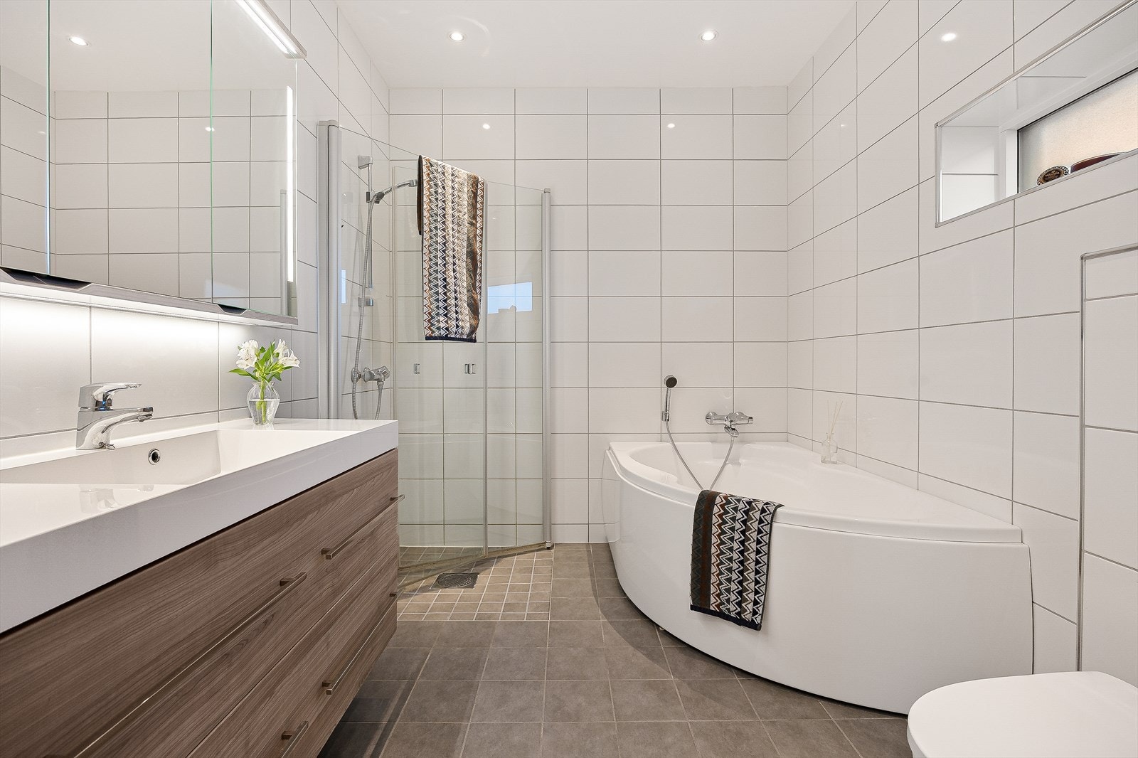 Videre fra walk-in closetet er det et eget bad. Badet er helfliset og innredet med moderne innredning samt hjørnebadekar. Her er det også varmekabler i gulvet. Galleribilde