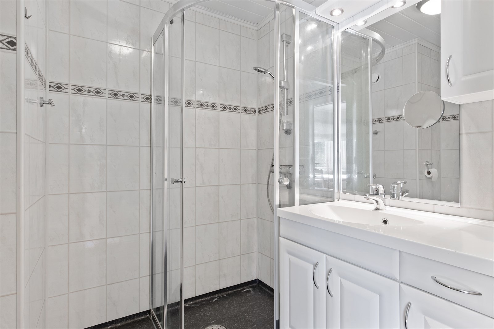 Badet er utstyrt med servantskap, speil med lysarmatur over og dusjhjørne. Galleribilde