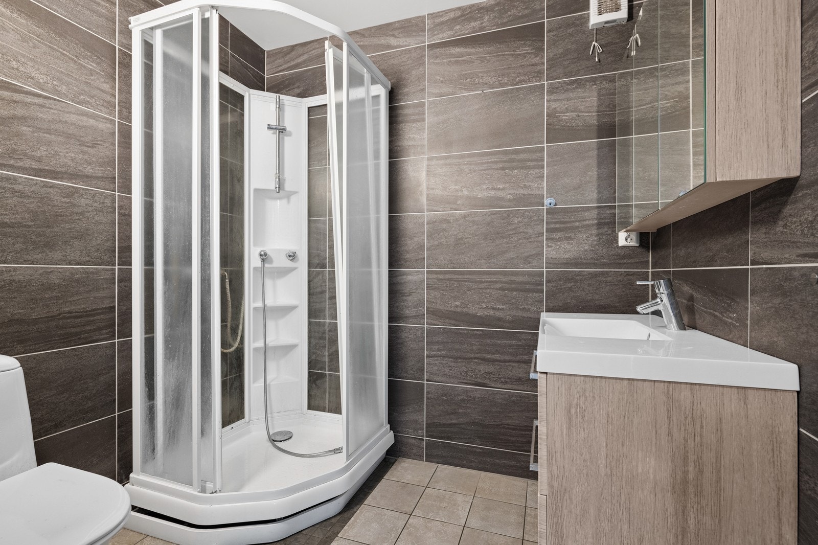 Badet er innredet med dusjakbinett, klosett, speilskap og servantskap. Galleribilde