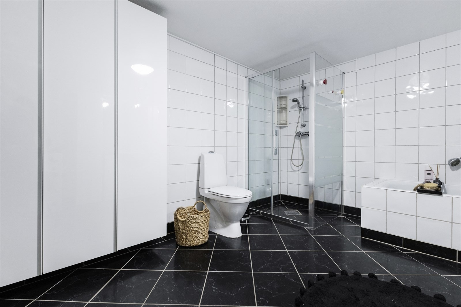 Badet er innredet med glatt baderomsinnredning med heldekkende servant nedfelt i underskap, speilskap med belysning, toalett, dusjhjørne med glassdører samt badekar. Galleribilde