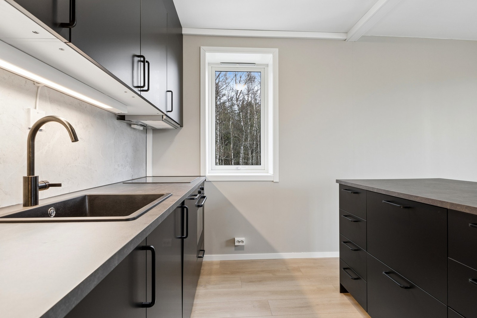 Du får en moderne og funksjonell kjøkkeninnredning med slette, sorte fronter og laminat benkeplate. Galleribilde